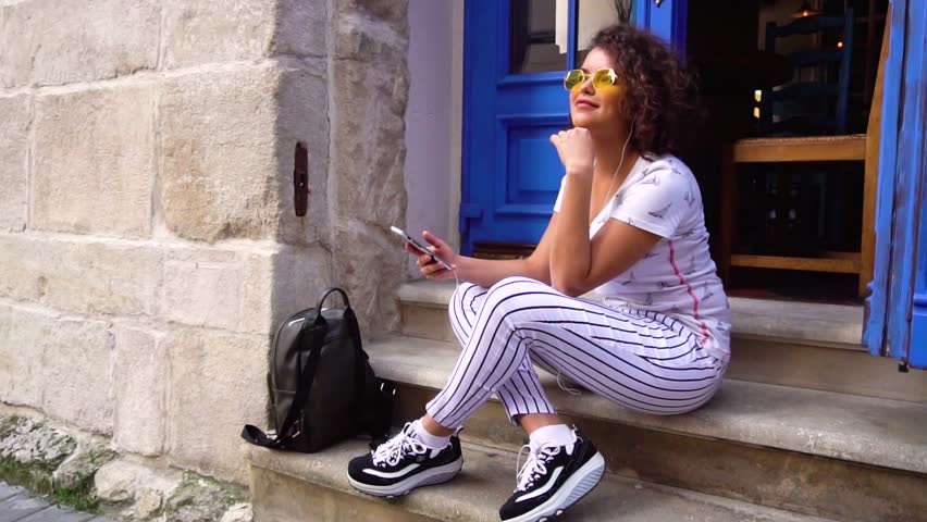 Young woman student sitting and using phone, listening to the music on stairs