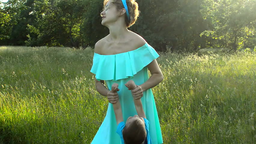 Mom twists a child on his hands in the street, outdoors in the evening sunshine