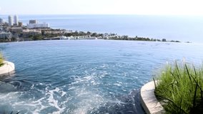 Video footage clip of water wave ripple in the infinity edge swimming pool with aerial view of ocean on beautiful summer daylight.

