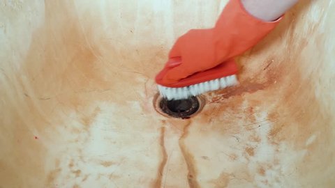 A man's hand in red rubber gloves cleans the bathroom sink with a scrub brush. General house cleaning. Closeup shot.