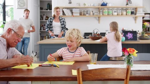 Grandad and grandson drawing together in busy family kitchen