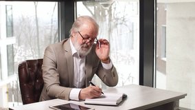 Old professor with grey hair and beard in beautiful suit taking notes in the notebook. - Powered by Shutterstock - Get 15% off with code: PIKWIZARD15