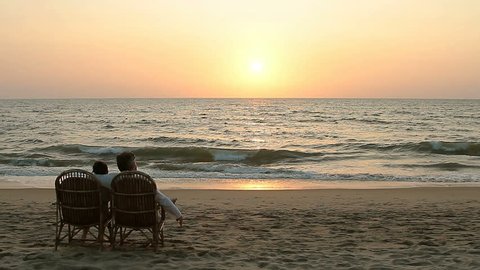 Loving couple enjoying the sunset, sitting in armchairs near the ocean coast line 库存视频