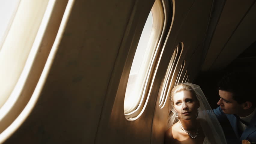 Close-up portrait of the handsome groom kissing his charming bride in the cheek while sitting near the window in the plane.