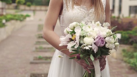 young girl in a wedding dress is holding a bouquet of the bride. Close-up. Wedding bouquet. Beautiful bridal bouquet in hands of young bride dressed in white wedding dress. slow motion.