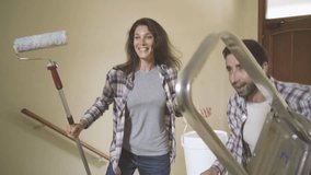 Young happy couple moving in their new house, they are painting walls, doing a home makeover, unpacking and toasting to celebrate: home renovation and real estate concept, video montage