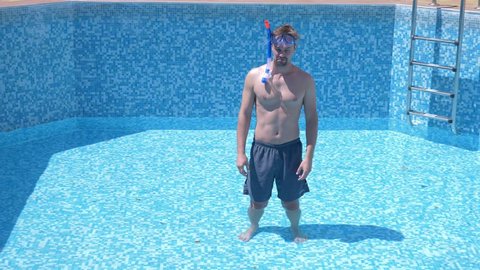 a young funny guy climbs into an empty swimming pool with a snorkelling mask and snorkel. 4k. humor.