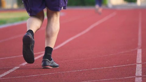 Low angle shot of an senior man's legs jogging on the stadium. Back view. Slow motion