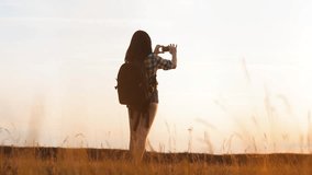 Hipster hiker silhouette girl is shooting video of beautiful nature sundown on smartphone slow motion video. 