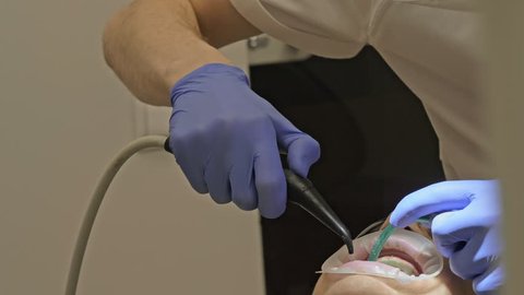 Dentist is treating a patient in a modern dental office. Orthodontist works with an assistant. The operation is carried out using a cofferdam. The client is inserted and restored teeth, make a denture