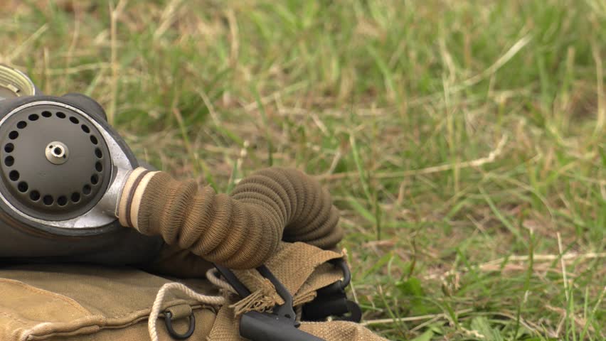 An old American gas mask lies on the blanket. Different equipment in the background. Green grass.