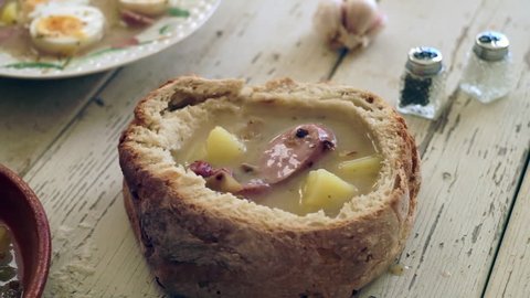 Pouring polish traditional soup called zur or white borscht into bread bowl