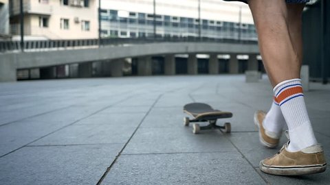 Male legs doing tricks on skateboard, skateboarder feet while skating in city, view from the back