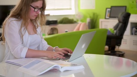 A wide shot of a female student writing an essay on a laptop at home.