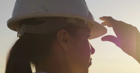 Slow motion close up of a woman engineer looking at the horizon proud of her work and putting a construction helmet on at sunset.Concept of: career, success, work and engineering.