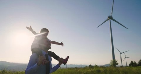 A father engineer, holds his daughter in his arms and runs between the wind turbines with great freedom. Concept of: environmental engineering, renewable energy and love for nature and for the family