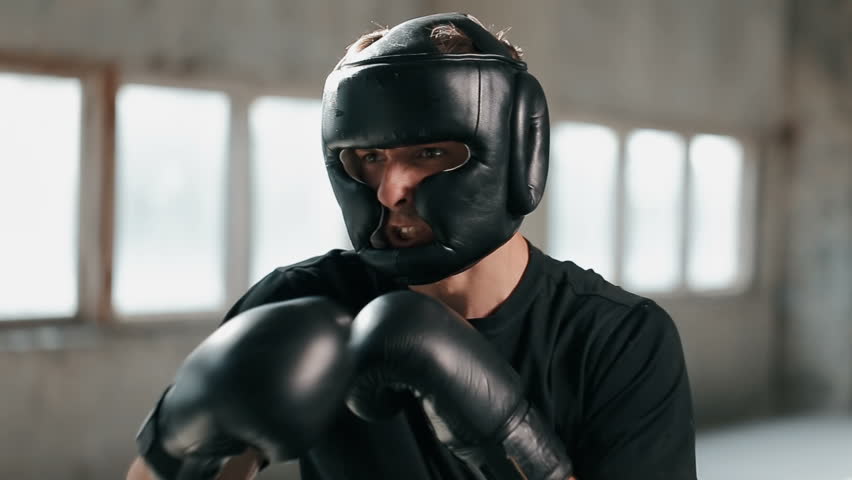 Fit boxer in black leather mask practises punching-defense techniques, indoor shot of daily workout in spacious light facilities | Shutterstock HD Video #1012506719