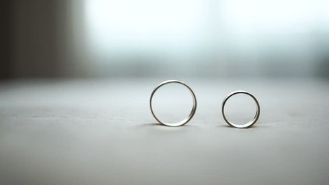 Composition of two wedding silver rings at the table. The male ring is rolling to another.