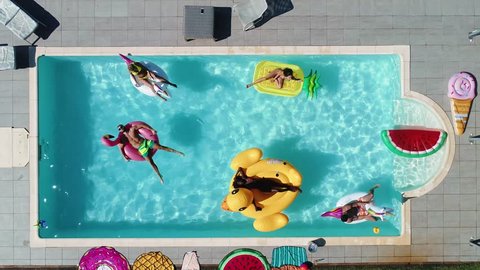 Group of friends having fun in the swimming pool with inflatable colored toys