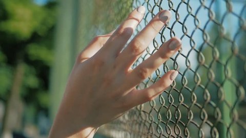 Female hand moving along the surface of grid. Arm of young woman touching metal wire fence. Girl walking during summer vacation and leading his fingers along the guard of bridge. Close up Slow motion