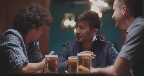 three young friends drinking beer in bar or pub 4k dollyshot