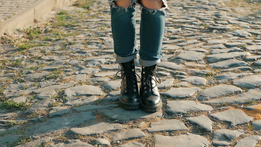 Closeup of young woman legs in black boots on cobblestone street