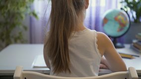 Unrecognizable little girl with long blond hair is doing her homework sitting in her room near a large window. School life concept. Slider real time close up shot