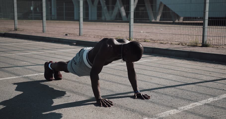 Street workout. Athletic African American man doing push-ups and spin exercise on outdoors. A black man is playing sports near the stadium. Workout, fitness, running, motivation | Shutterstock HD Video #1012521941