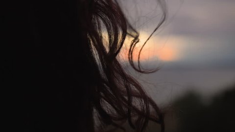 Woman's Wavy/Curly Dark Hair in Front of Cloudy Sunset in Slow Motion. A Lonely or Isolated Feeling is Being Suggested in the Clip.