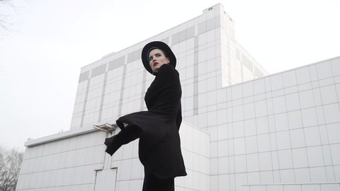 Girl in a black tunic, cloak and hat turns around in front of white minimalistic building. Turns around and waving her dress. Slow motion shot 120 fps.