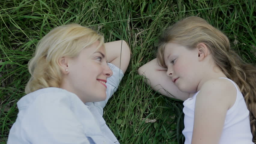 Loving mother lying on grass with little daughter. Looking at each other