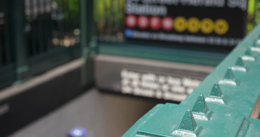 A slow dollying shot of people entering and exiting a New York City Manhattan underground subway station. Extreme shallow DOF with focus point on railing.  	