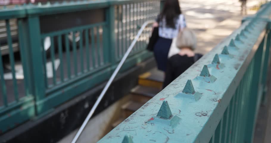 A slow dollying shot of people entering and exiting a New York City Manhattan underground subway station. Extreme shallow DOF with focus point on railing.  	