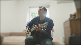 Handsome young musician playing the guitar and singing. Man Playing Acoustic Guitar Close Up slow motion video. in the room sits lifestyle on the couch. man and guitar concept