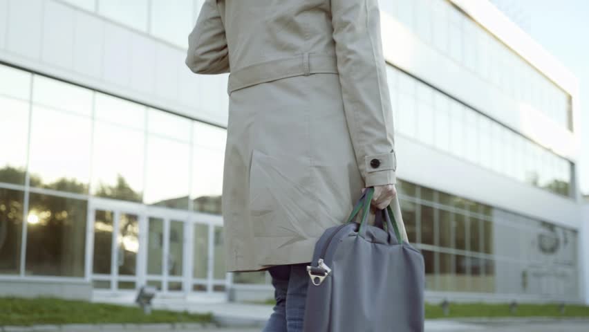 A woman with a bag in her hand is walking on the background of a glass facade.