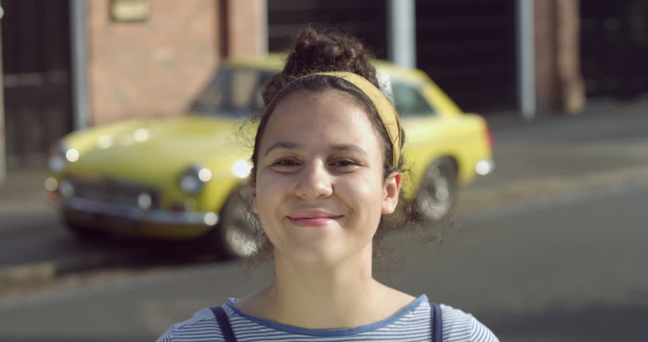 Portrait of Retro Smiling Mixed Race Teenage Girl with Headscarf next to a Vintage Yellow Car. Curly Afro Hair Dual Heritage ethnic Woman on a London City Street. A Hipster Tourist Student in Britain.