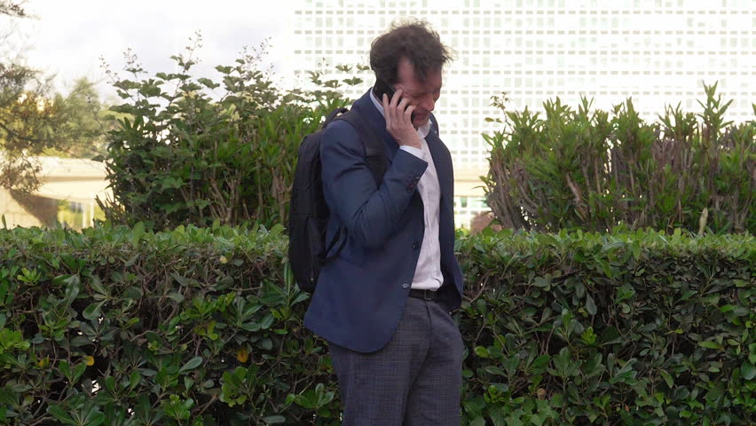 Happy professor with suit and backpack talking on the phone smiling 