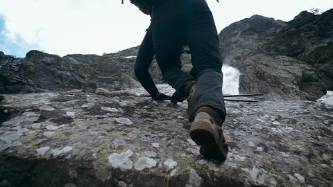Man climbs on a rock to a mountain waterfall. A climber climbs a boulder to a huge waterfall