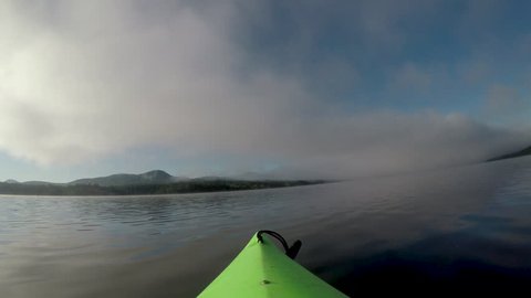 POV of the tip of a kayak drifting or floating in a calm mountain lake or river as the mist or fog burns off in the morning