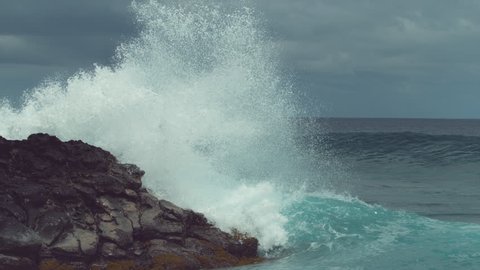 SLOW MOTION: Emerald breaking wave hits the rocky coast with incredible force and splashes high into the air, sending droplets of crystal clear seawater everywhere. Powerful waves near Easter Island.