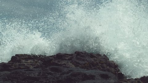 SLOW MOTION, CLOSE UP: Powerful ocean swell hits the tropical black rocky shore and splashes high in the air. Spectacular view of dangerous waves crashing into the tropical beach on Easter Island.