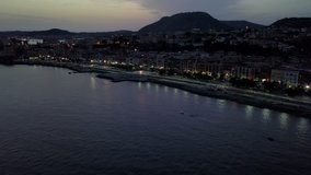 Aerial drone video of the Italian city of Pozzuoli at night.  It is a beautiful coastal city and tourist destination next to Naples.  Drone flies over the water with the city lights reflecting.