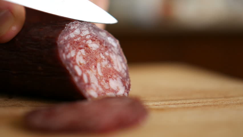 Man cuts into thin slices fatty sausage. Shooting closeup. Chef cutting salami with a knife on a wood board close up.  | Shutterstock HD Video #1012587749