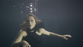 Pretty woman in black dress swimming like mermaid underwater pool
