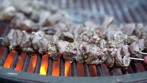 Raw lamb shish kabobs with sesame seeds on them on a hot, smoking grill with cameraing to the left.