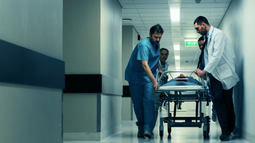 Emergency Department: Doctors, Nurses and Paramedics Push Gurney  Stretcher with Seriously Injured Patient towards the Operating Room. Shot on RED EPIC-W 8K Helium Cinema Camera.