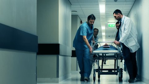 Emergency Department: Doctors, Nurses and Paramedics Push Gurney  Stretcher with Seriously Injured Patient towards the Operating Room. Shot on RED EPIC-W 8K Helium Cinema Camera.