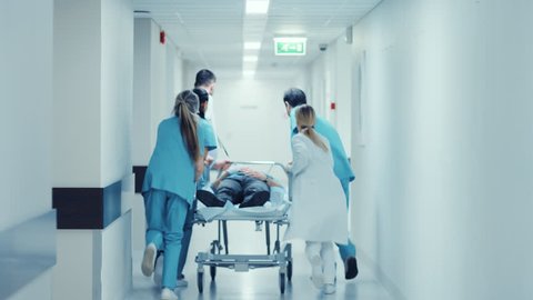 Emergency Department: Doctors, Nurses and Paramedics Run and Push Gurney / Stretcher with Seriously Injured Patient towards the Operating Room. Shot on RED EPIC-W 8K Helium Cinema Camera.
