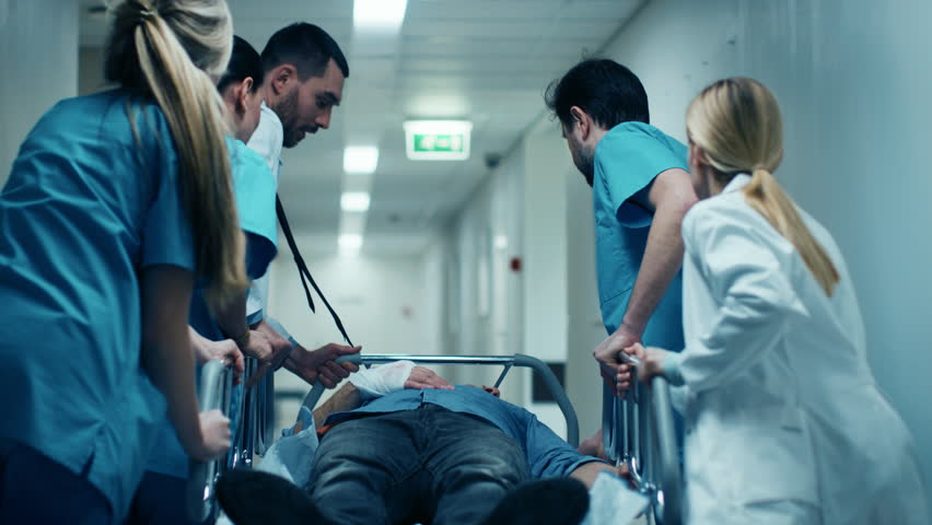 Emergency Department: Doctors, Nurses and Surgeons Move Seriously Injured Patient Lying on a Stretcher Through Hospital Corridors. Medical Staff in a Hurry Move Patient into Operating Theater. 4k UHD.