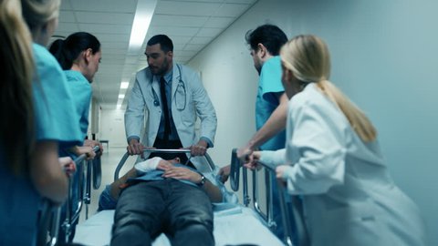 Emergency Department Doctors, Nurses and Surgeons Move Seriously Injured Patient Lying on a Gurney Through Hospital Corridors. Medical Staff in a Hurry Move Patient into Operating Theater. 4K UHD.